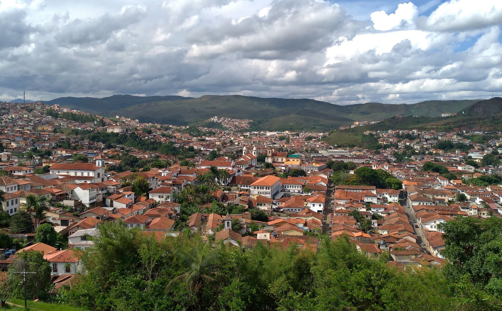 Vista panorâmica do centro histórico de Mariana, com telhados de telha, torres de igrejas e as montanhas de Minas ao fundo
